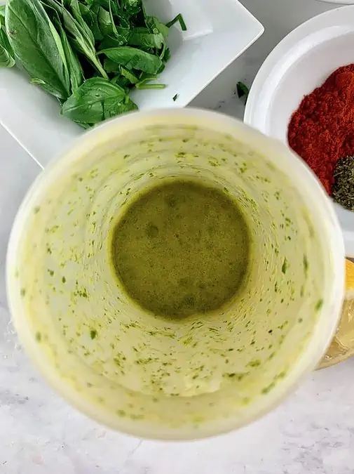 Italian vinaigrette ingredients blitzed in a blender with basil and herbs in background.