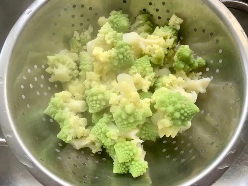 DRAINING ROMANESCO IN A STAINLESS COLANDER IN SINK