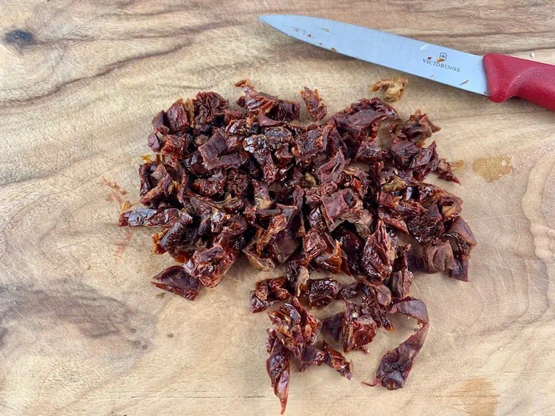 DICING DRIED TOMATOES WITH KNIFE ON WOODEN BOARD