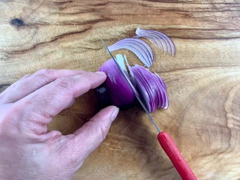THINLY SLICING RED ONION ON WOODEN BOARD WITH RED KNIFE