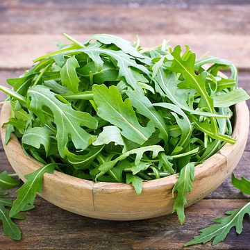 Baby arugula or rocket in a bowl on a wooden background