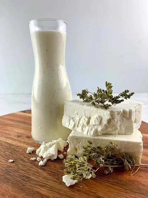 FETA DRESSING IN GLASS CONTAINER ON A WOODEN BOARD WITH FETTA & DRIED OREGANO