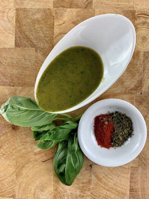 Blitzed Italian vinaigrette in a white bowl with fresh basil and paprika and dried oregano in a white bowl on the side.
