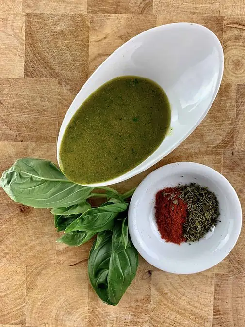 Italian vinaigrette in a white bowl with fresh basil and paprika and dried oregano in a white bowl on the side.