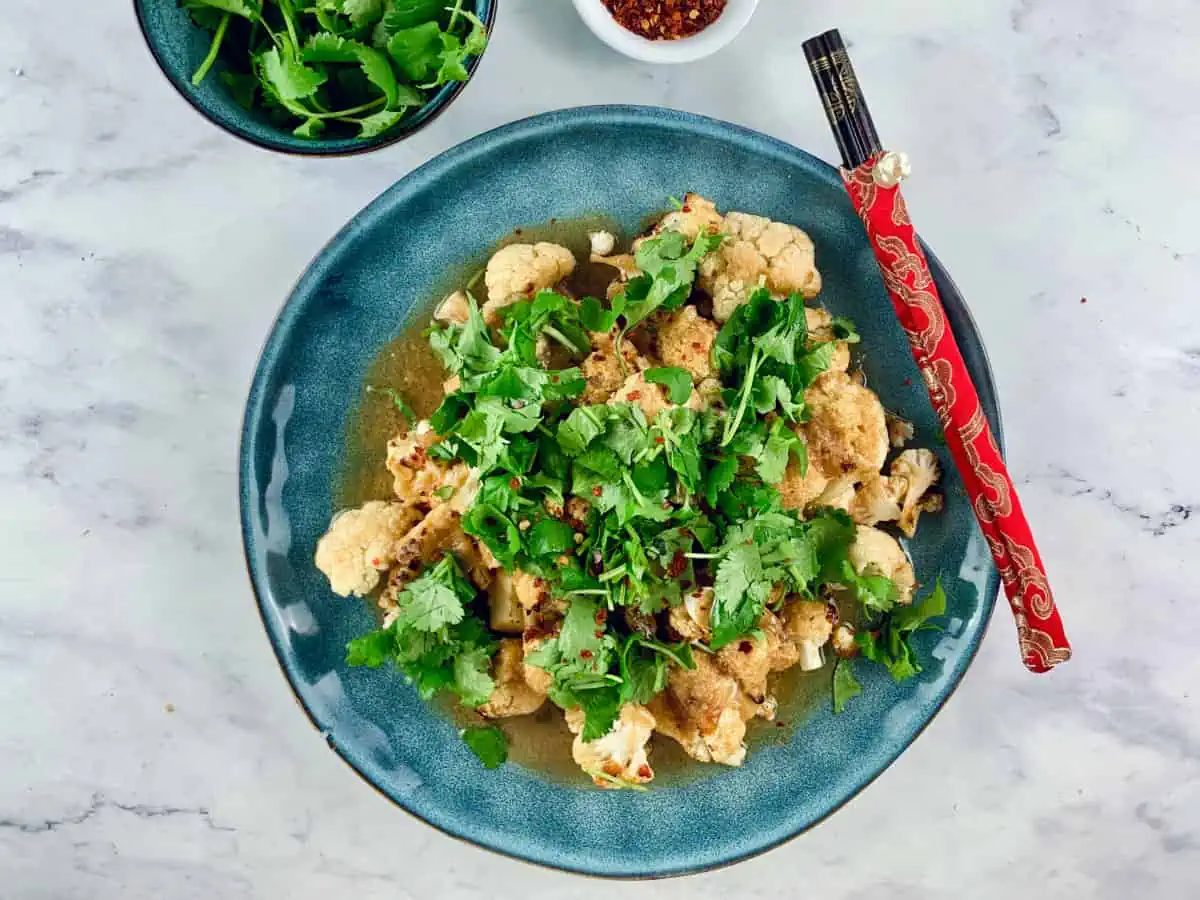 MISO CAULIFLOWER IN BLUE BOWL WITH CHOPSTICKS, CHILLI FLAKES & CORIANDER ON THE SIDE