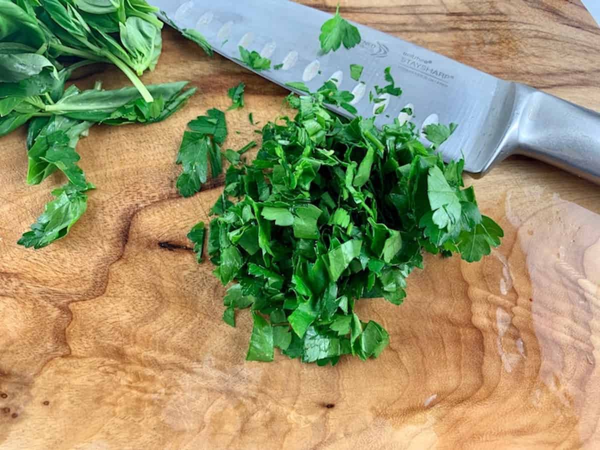 Roughly chopping parsley leaves on a wooden board with a knife.