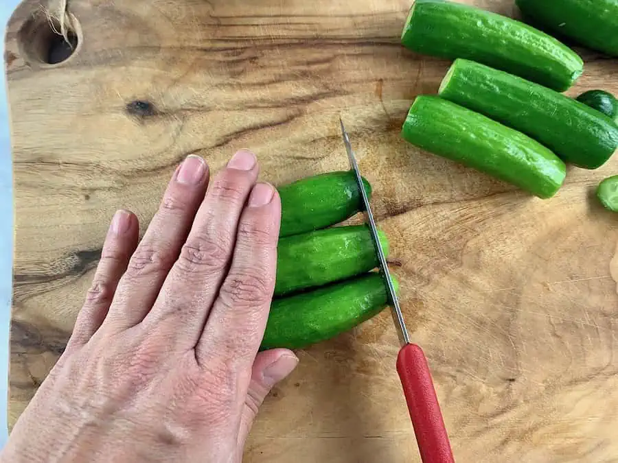 TRIMMING ENDS FROM CUKES ON WOODEN BOARD WITH RED KNIFE