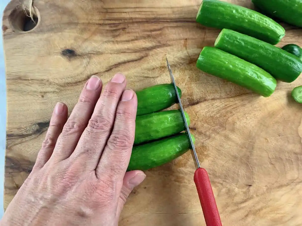 Trimming ends from cukes on wooden board with red knife.