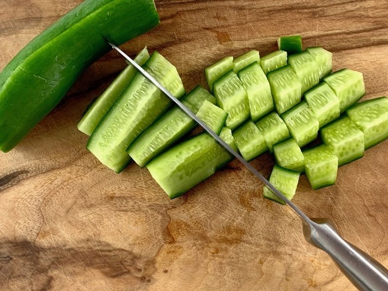 DICING CUCUMBERS ON A WOODEN BOARD WITH A KNIFE