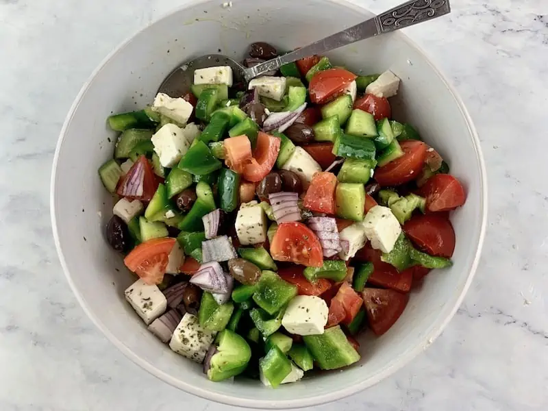 MIXING KETO GREEK SALAD WITH A SPOON IN A WHITE BOWL