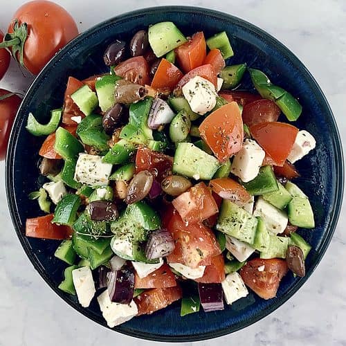 KETO GREEK SALAD IN A BLUE BOWL WITH SPOONS AND TOMATOES ON THE SIDE