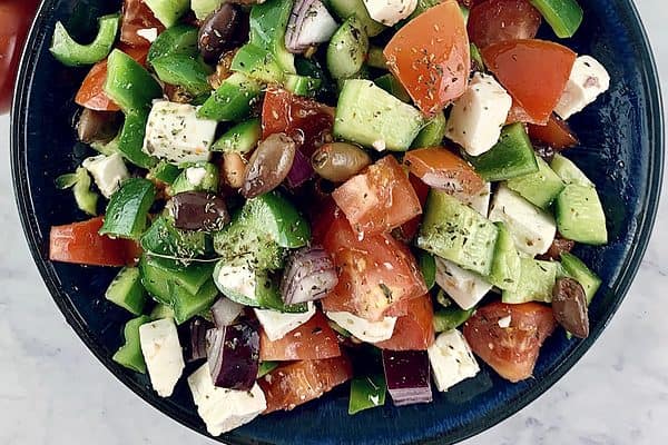 Keto Greek salad in a blue bowl with spoons and tomatoes on the side.