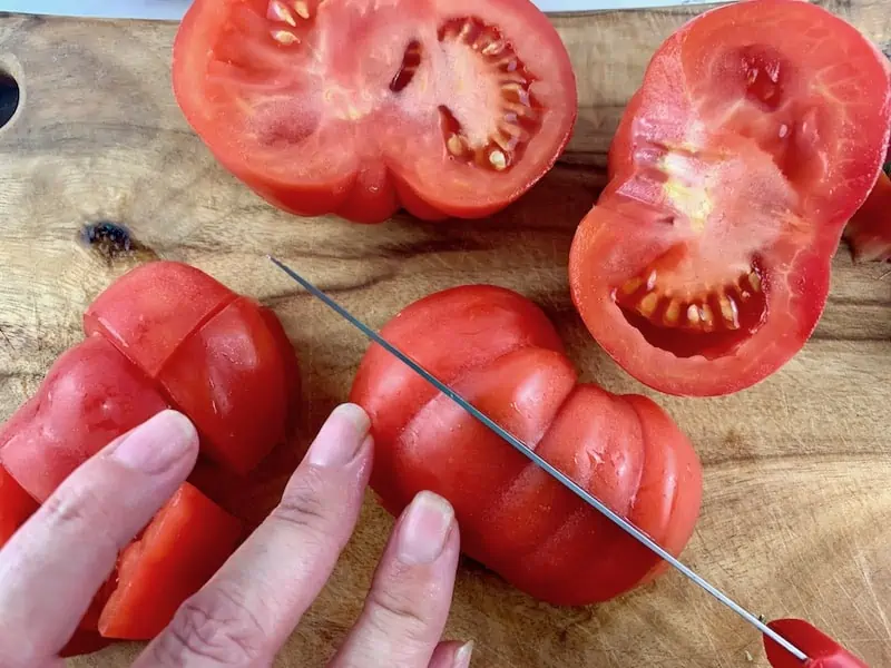 HANDS CUTTING HEIRLOOM TOMATOES INTO CUNKS WITH A KNIFE ON A WOODEN BOARD