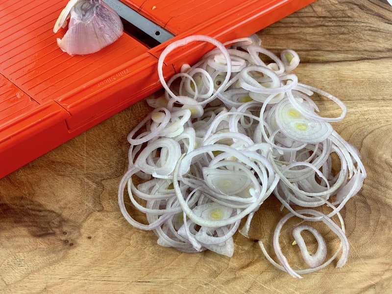 THINLY SLICING FRENCH SHALLOTS WITH A MANDOLINE SLICER ON A WOODEN BOARD