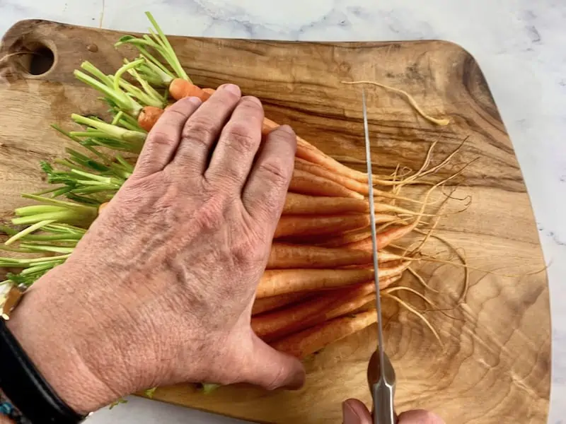 HANDS LINING BABY CARROTS UP ON A WOODEN BOARD TO BE TRIMMED WITH A KNIFE