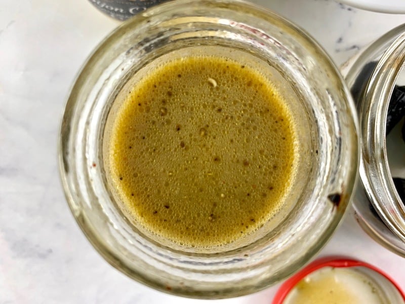 Shaken black garlic vinaigrette in a glass jar with ingredients surrounding it.