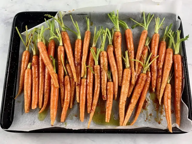 TRIMMED BABY CARROTS ON A LINED BAKING TRAY WITH SPICES AND OIL