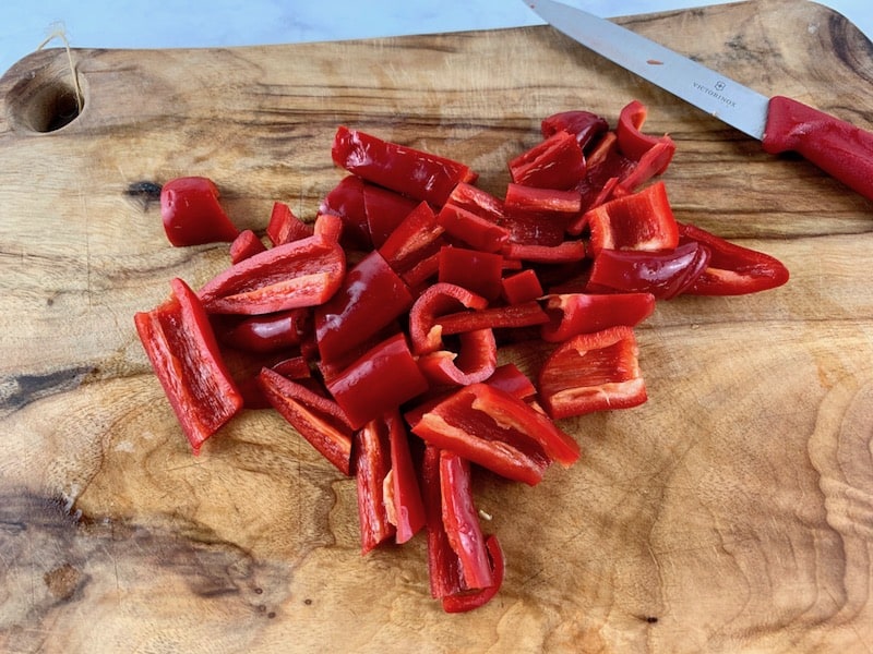 ROUGHLY CHOPPING CHILLIS ON A WOODEN BOARD WITH A RED KNIFE