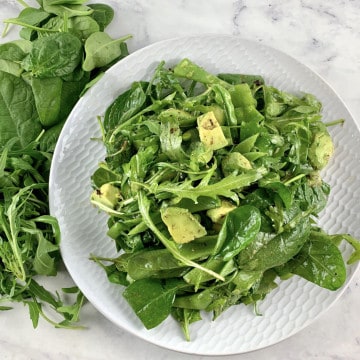 SPINACH ARUGULA SALAD ON A WHITE PLATE WITH GREENS SCATTERED AROUND