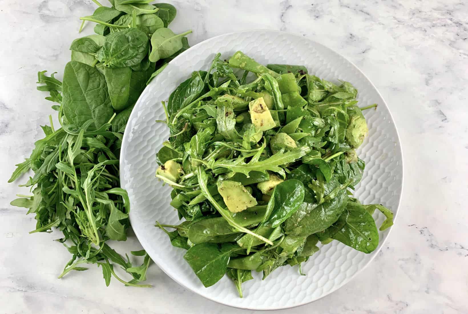 SPINACH ARUGULA SALAD ON A WHITE PLATE WITH GREENS SCATTERED AROUND