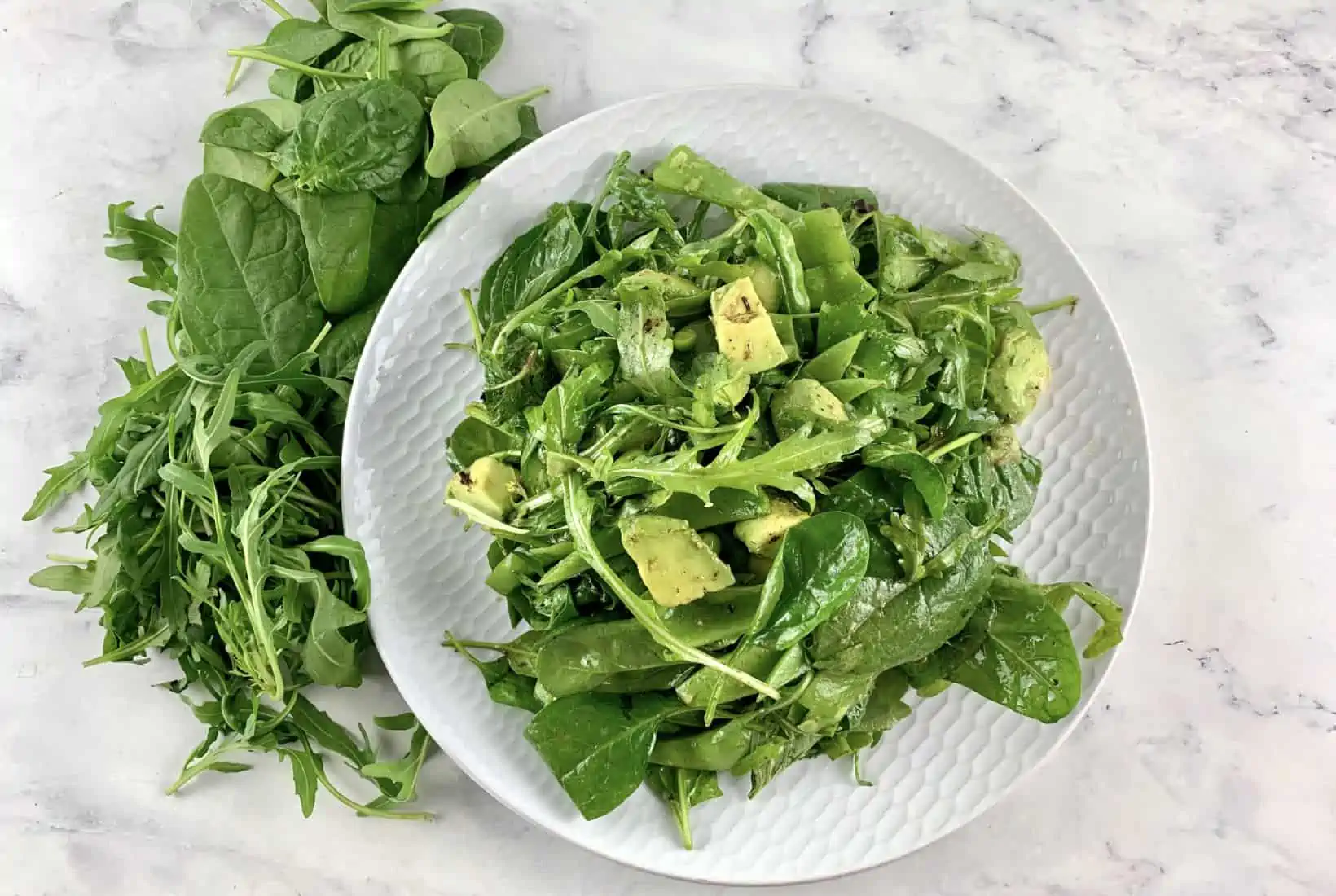 Spinach arugula salad on a white plate with greens scattered around.