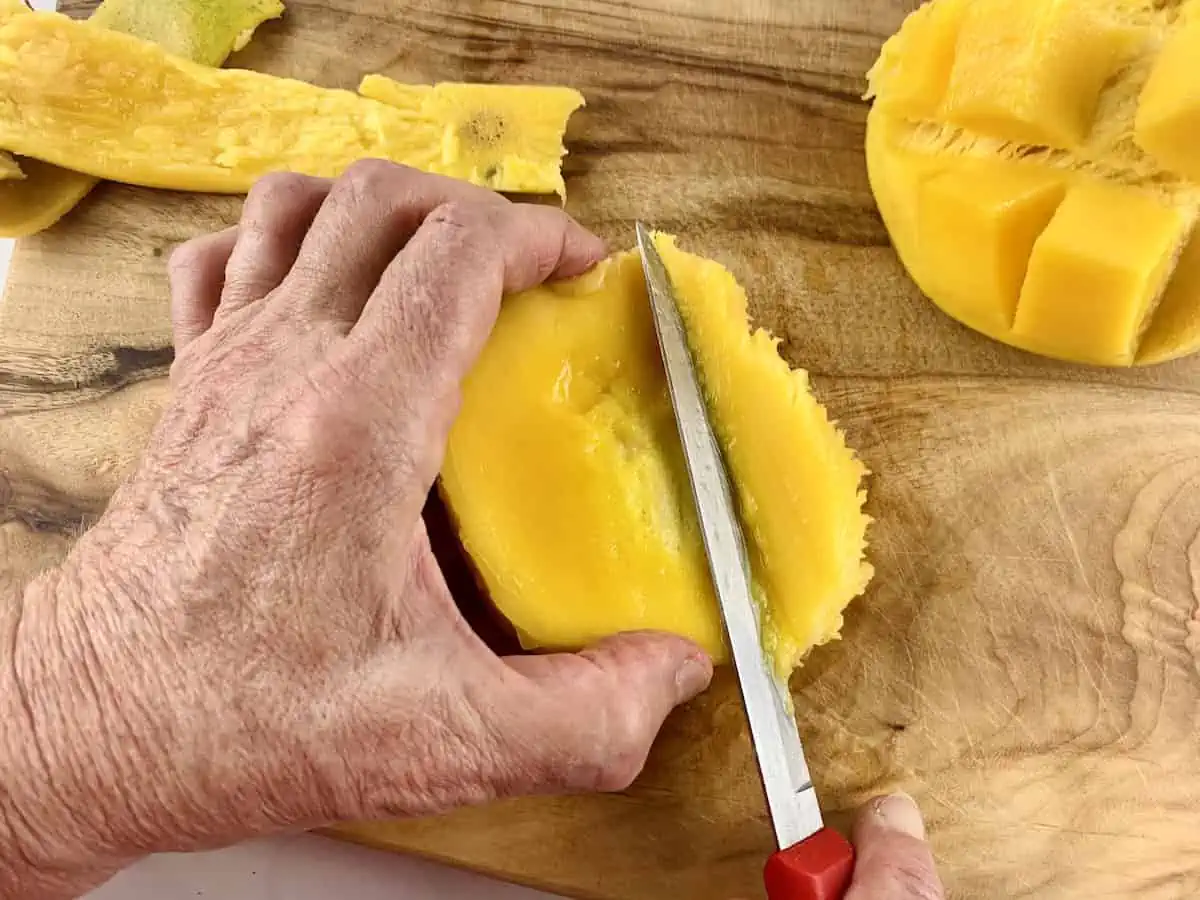 Hands are cutting around a mango seed on a wooden board with a knife.