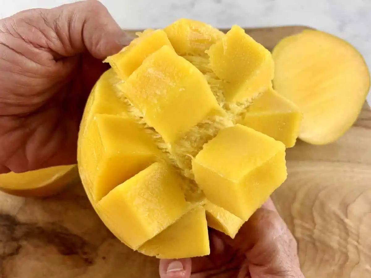 Hands flipping out diced mango cheek on wooden board.