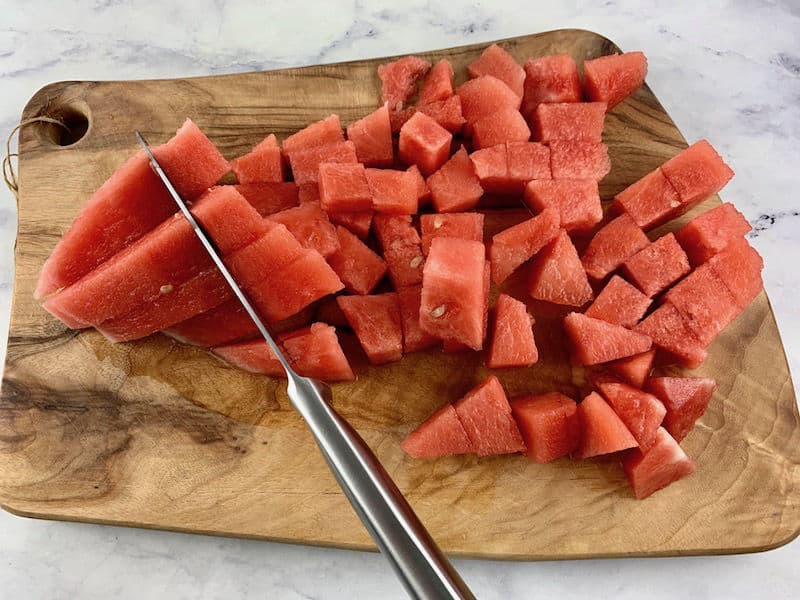 DICING WATERMELON WITH A KNIFE ON A WOODEN BOARD