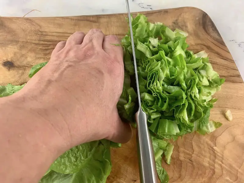 SHREDDING LETTUCE ON A WOODEN CHOPPING BOARD WITH A KNIFE