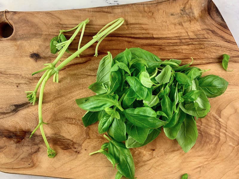 STRIPPING BASIL LEAVES FROM STEMS ON A WOODEN BOARD