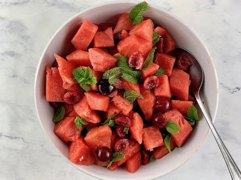 MIXING WATERMELON FRUIT SALAD IN A WHITE BOWL WITH A SPOON