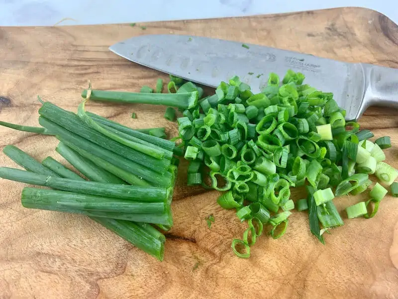 SLICING GREEN ONIONS ON A WOODEN CHOPPING BOARD WITH KNIFE