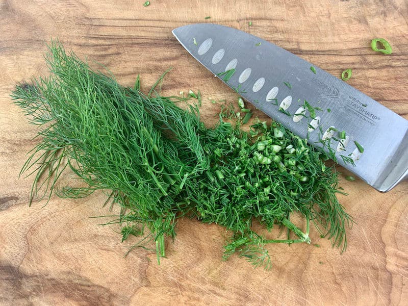 CHOPPING DILL ON A WOODEN CHOPPING BOARD WITH KNIFE