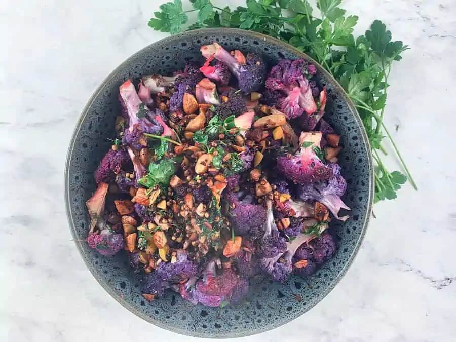 Purple cauliflower salad in a dark grey bowl with parsley on the side.