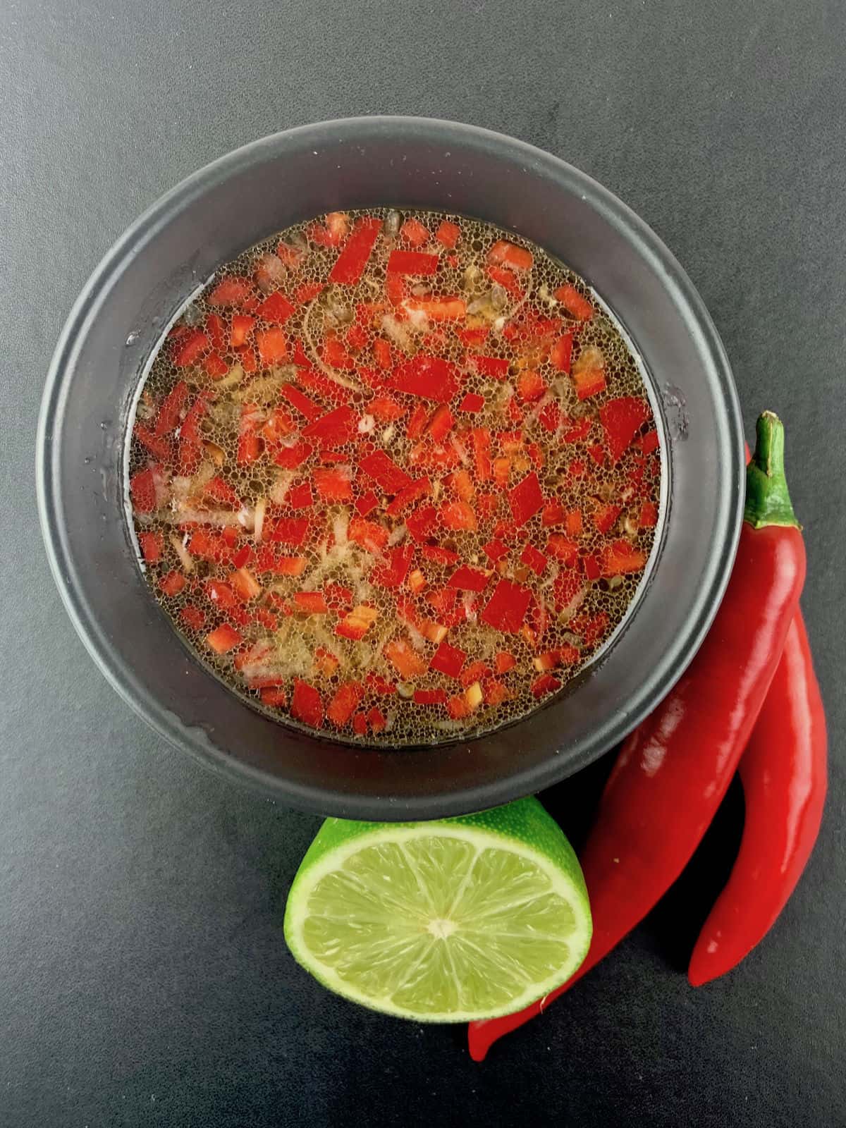 VIETNAMESE SALAD DRESSING IN BLACK BOWL WITH RED CHILLIES AND CUT LIME ON THE SIDE