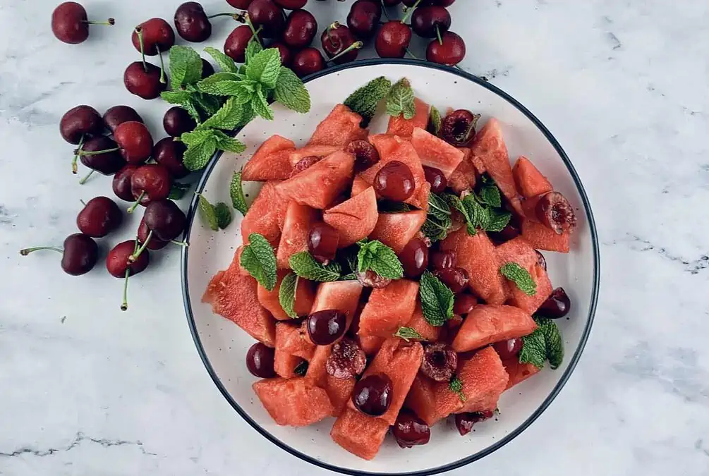 WATERMELON FRUIT SALAD ON A PLATTER WITH CHERRIES AND MINT ON THE SIDE