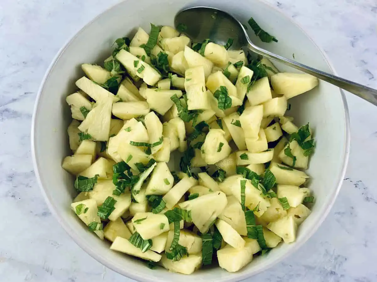 Mixing fresh pineapple and mint salad in a white bowl with a spoon.