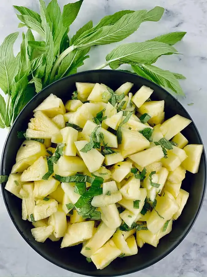 FRESH PINEAPPLE & MINT SALAD IN A BLACK BOWL WITH MINT LEAVES ON THE SIDE