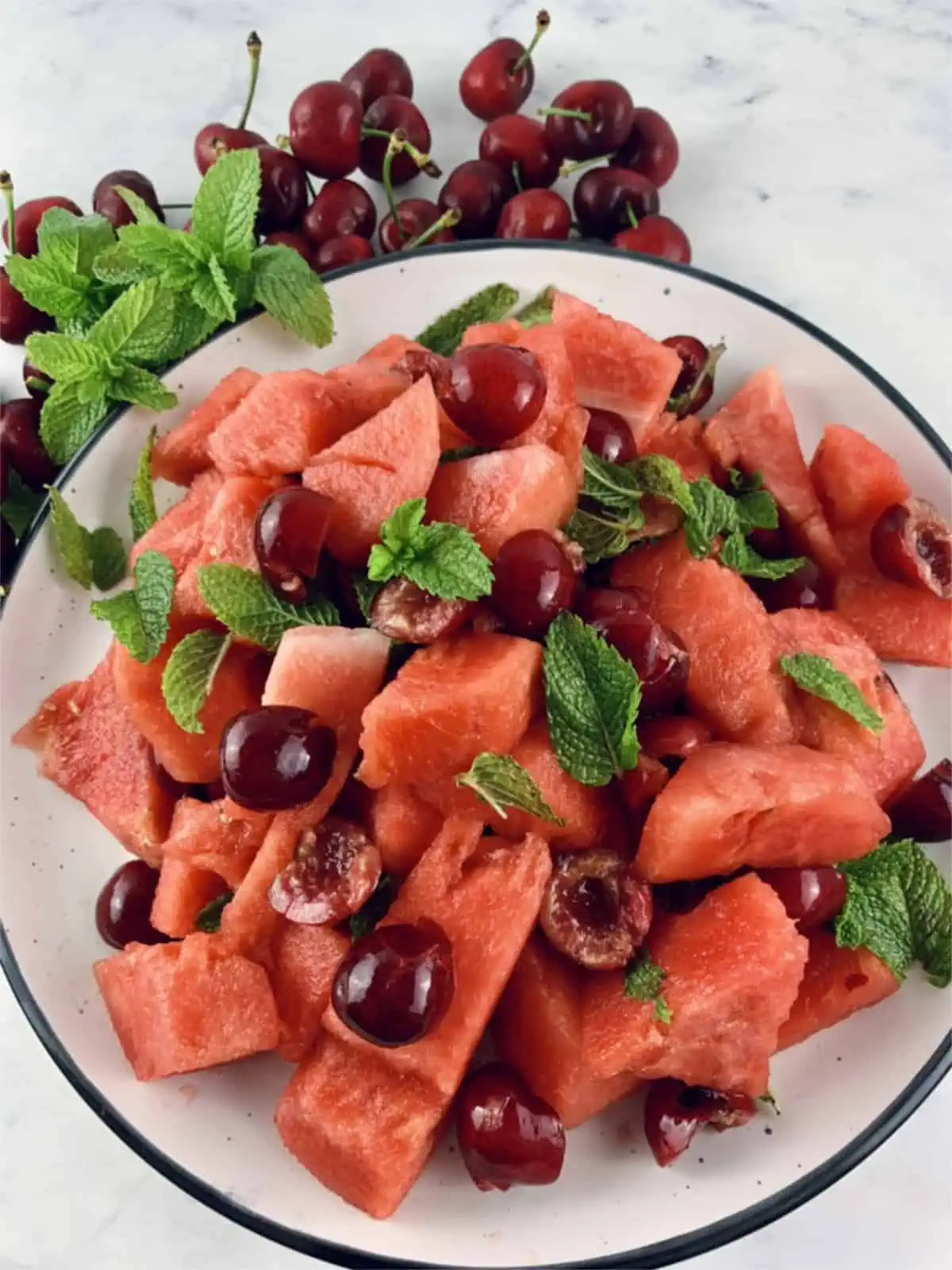 Watermelon fruit salad on a platter with cherries and mint on the side.