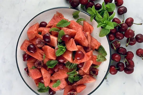 Watermelon fruit salad on a platter with cherries and mint on the side.