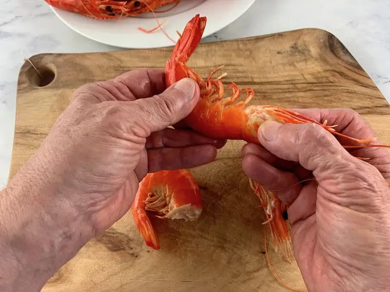 hands removing the head of a cooked prawn on wooden board