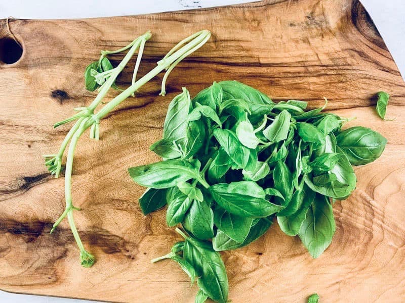 Basil leaves on a wooden chopping board that have been stripped from their stems.