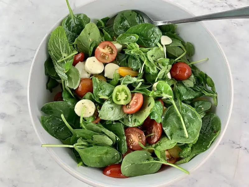 MIXING SPINACH CAPRESE,SALAD IN A WHITE WITH SPOON