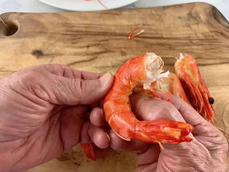 hands removing the legs of a cooked prawn on wooden board
