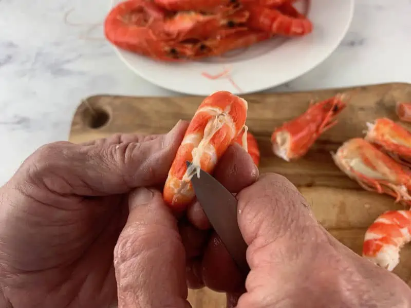 hands pulling out the vein of a cooked prawn with a knife