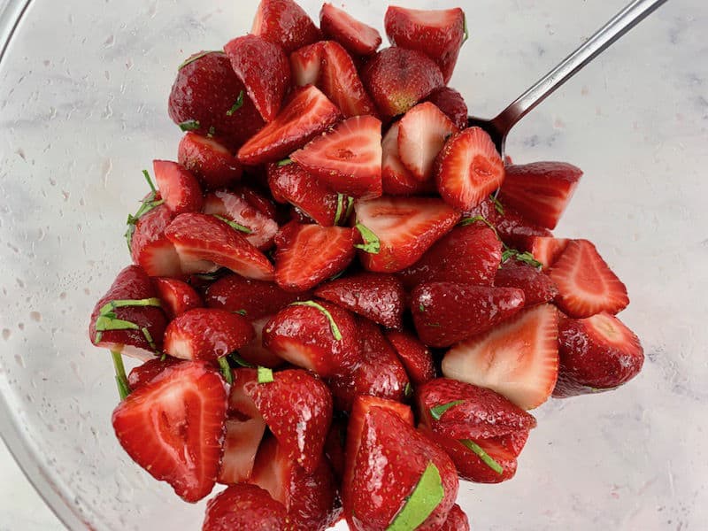 MIXING STRAWBERRIES AND LIME LEAVES IN A GLASS BOWL WITH A SPOON
