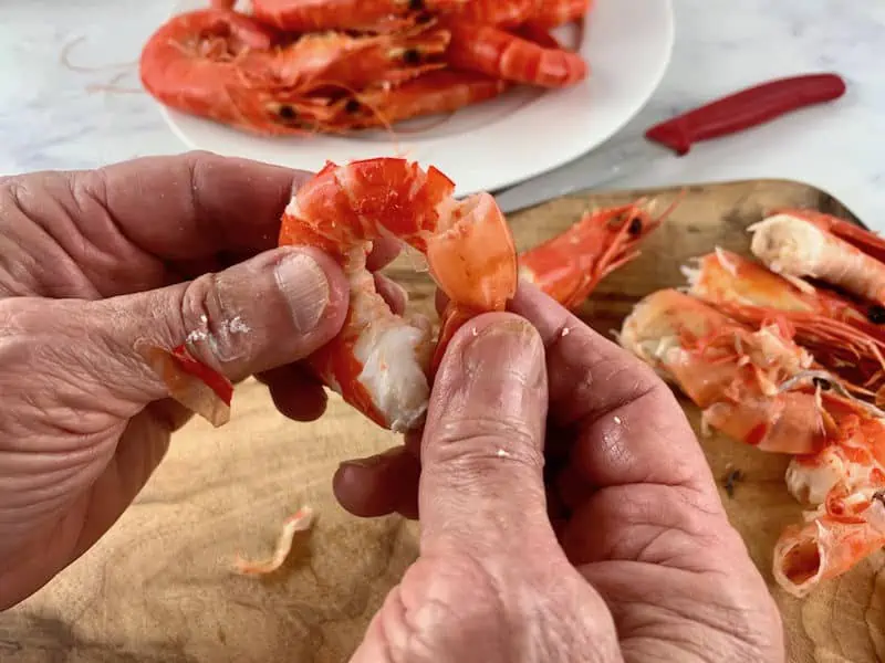 hands squeezing the tail of a cooked prawn to remove it