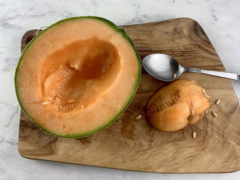 HALF MELON ON BOARD WITH SCOOPED OUT SEEDS AND SPOON ON SIDE