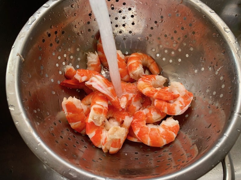 PEELED SHRIMP IN A COLANDER IN THE SINK WITH COLD RUNNING WATER