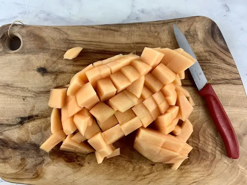 DICED MELON ON WOODEN BOARD WITH KNIFE ON THE SIDE